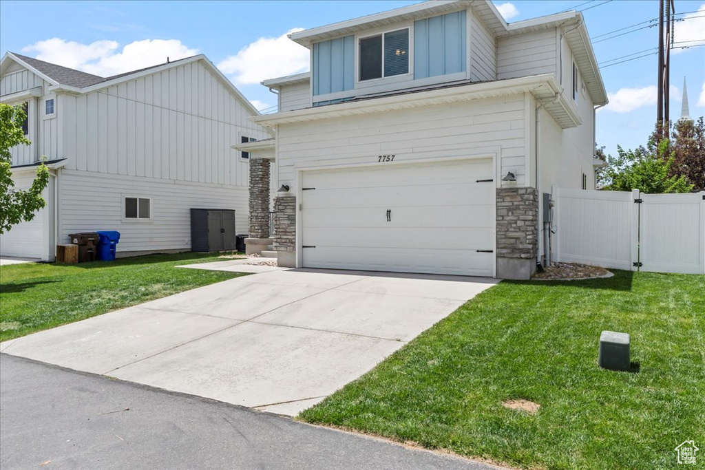View of front facade with board and batten siding, stone siding, an attached garage, and driveway