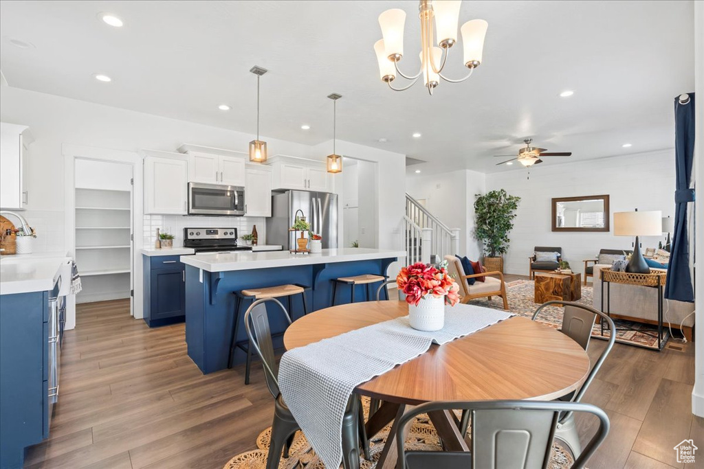 Dining room with a ceiling fan, stairway, wood finished floors, recessed lighting, and a chandelier