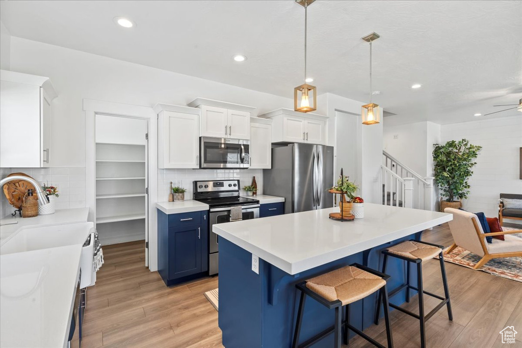 Kitchen featuring stainless steel appliances, blue cabinets, a breakfast bar, light wood-type flooring, and recessed lighting