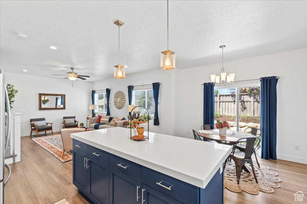 Kitchen featuring blue cabinetry, light wood-type flooring, a chandelier, light countertops, and decorative light fixtures