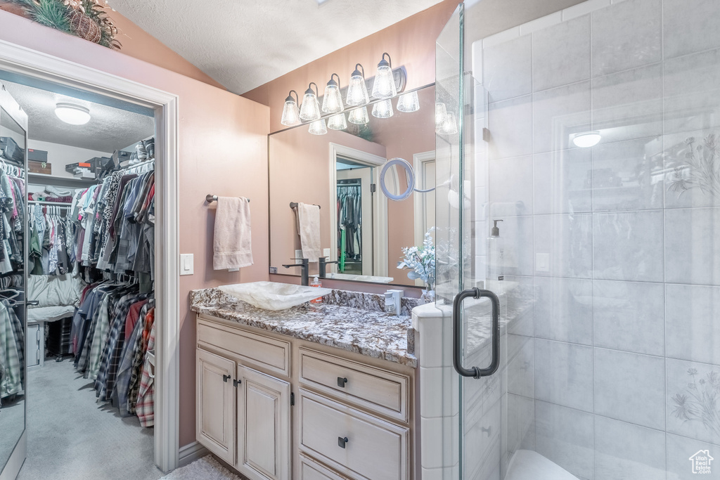 Bathroom featuring vanity, a walk in closet, a shower stall, lofted ceiling, and a textured ceiling