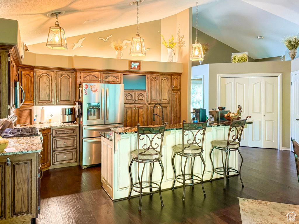 Kitchen featuring appliances with stainless steel finishes, brown cabinets, high vaulted ceiling, a breakfast bar area, and hanging light fixtures