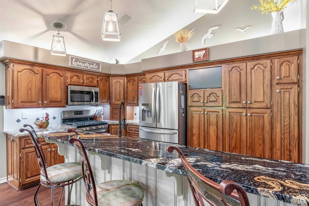 Kitchen with appliances with stainless steel finishes, lofted ceiling, brown cabinets, decorative backsplash, and dark wood-style flooring
