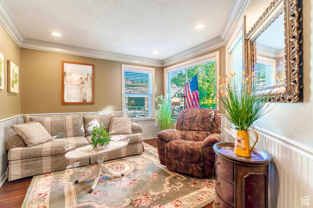 Living area featuring wood finished floors, healthy amount of natural light, a textured ceiling, wainscoting, and ornamental molding