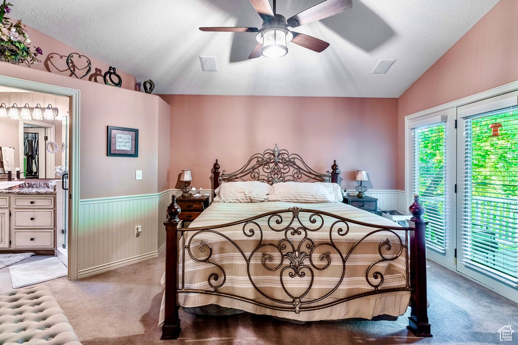 Bedroom featuring vaulted ceiling, a wainscoted wall, access to exterior, light carpet, and ensuite bathroom