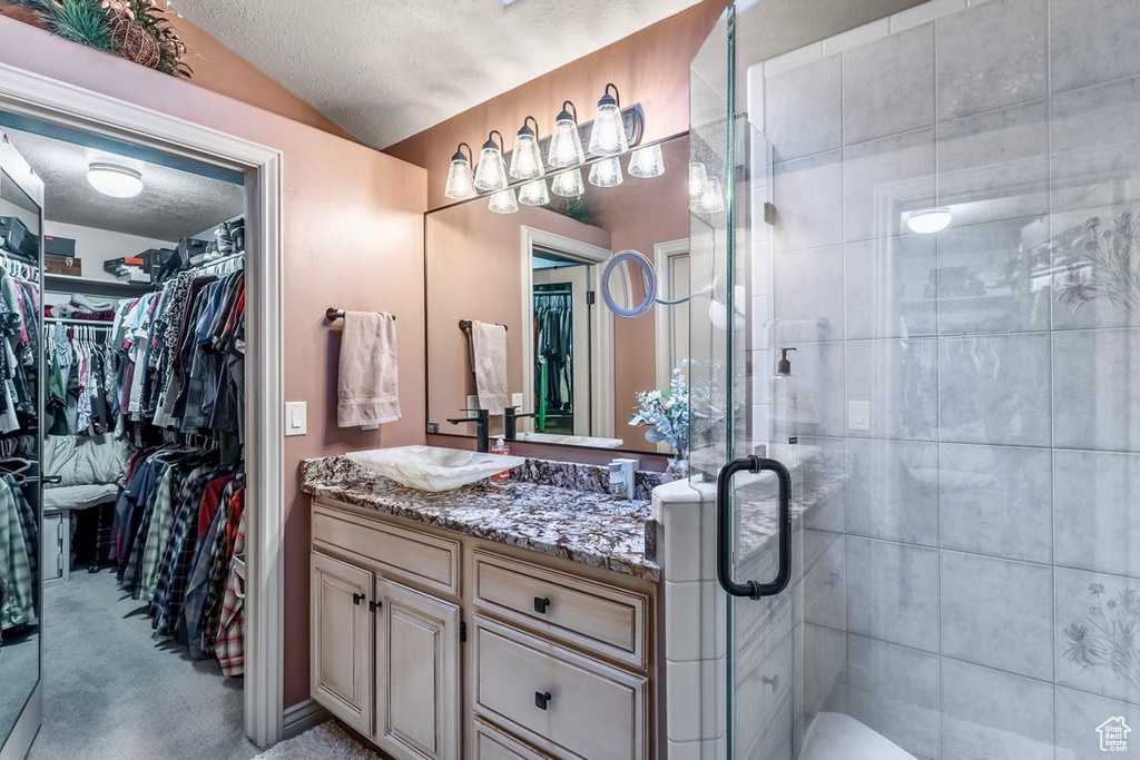 Bathroom featuring vanity, a walk in closet, a shower stall, a textured ceiling, and lofted ceiling