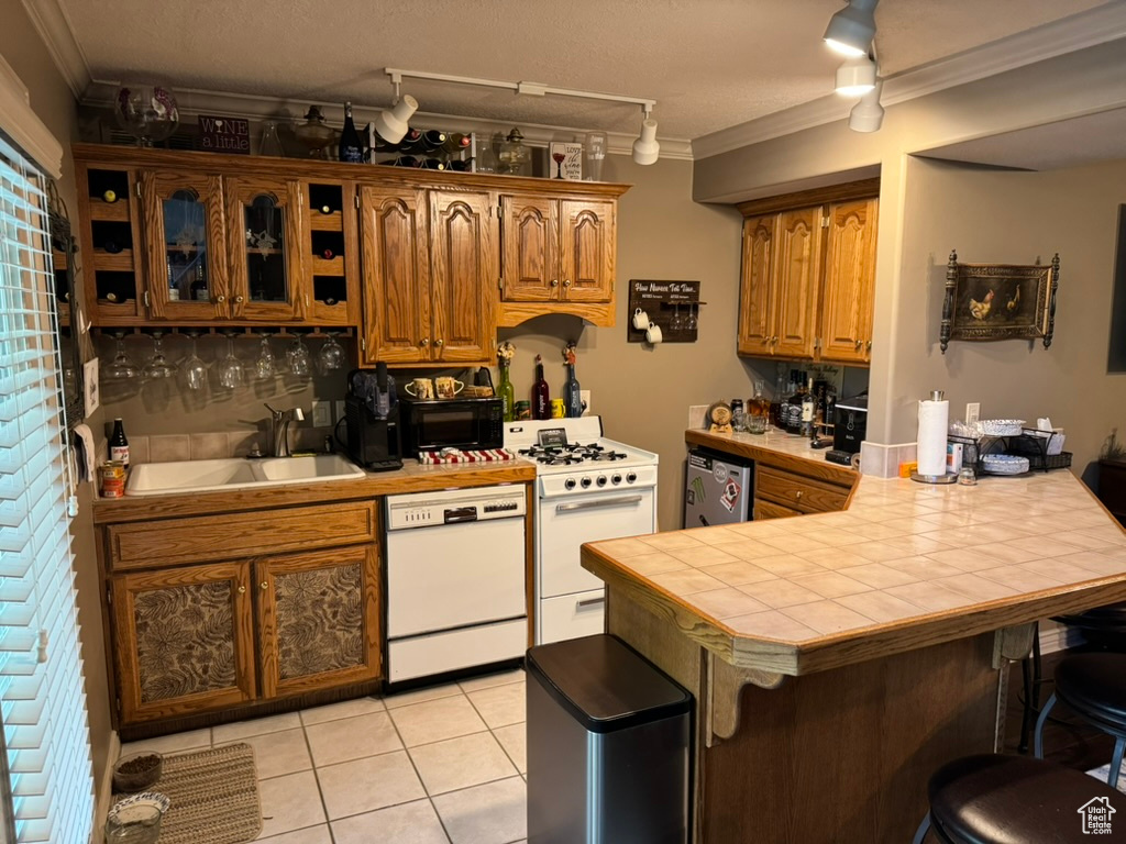 Kitchen featuring white appliances, crown molding, a kitchen breakfast bar, tile countertops, and a peninsula