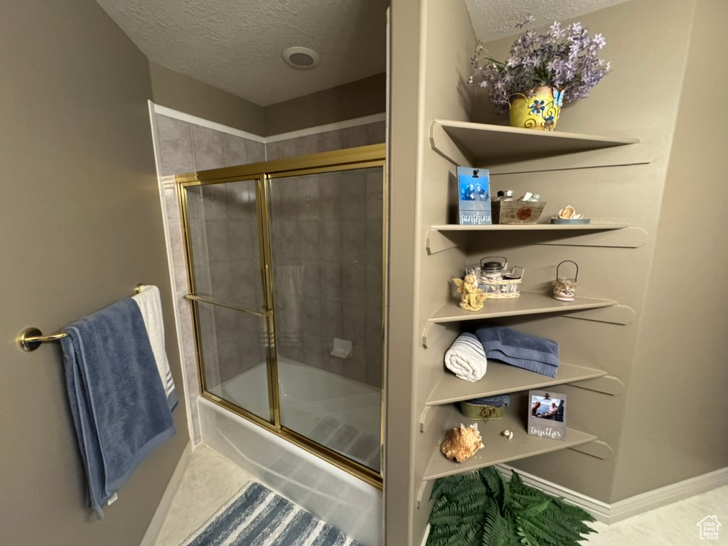 Bathroom with a textured ceiling and bath / shower combo with glass door