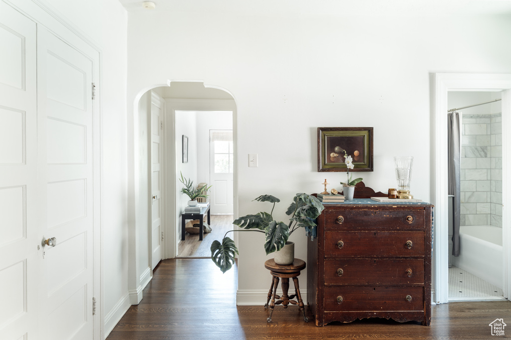 Hallway with arched walkways, dark wood-style flooring, and baseboards