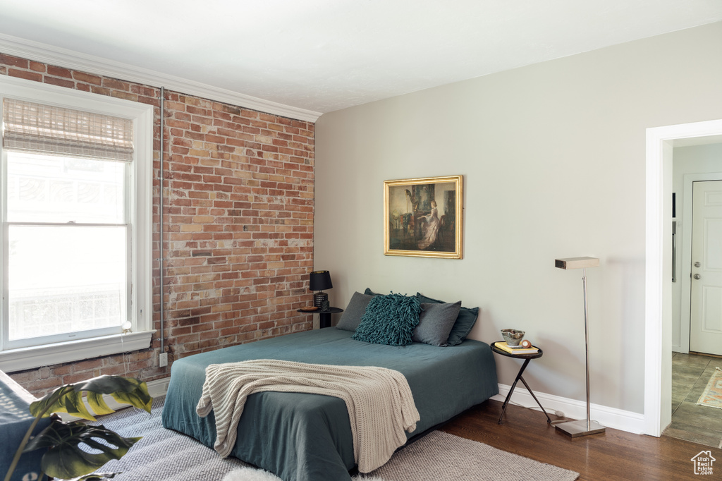 Bedroom featuring wood finished floors, brick wall, and baseboards