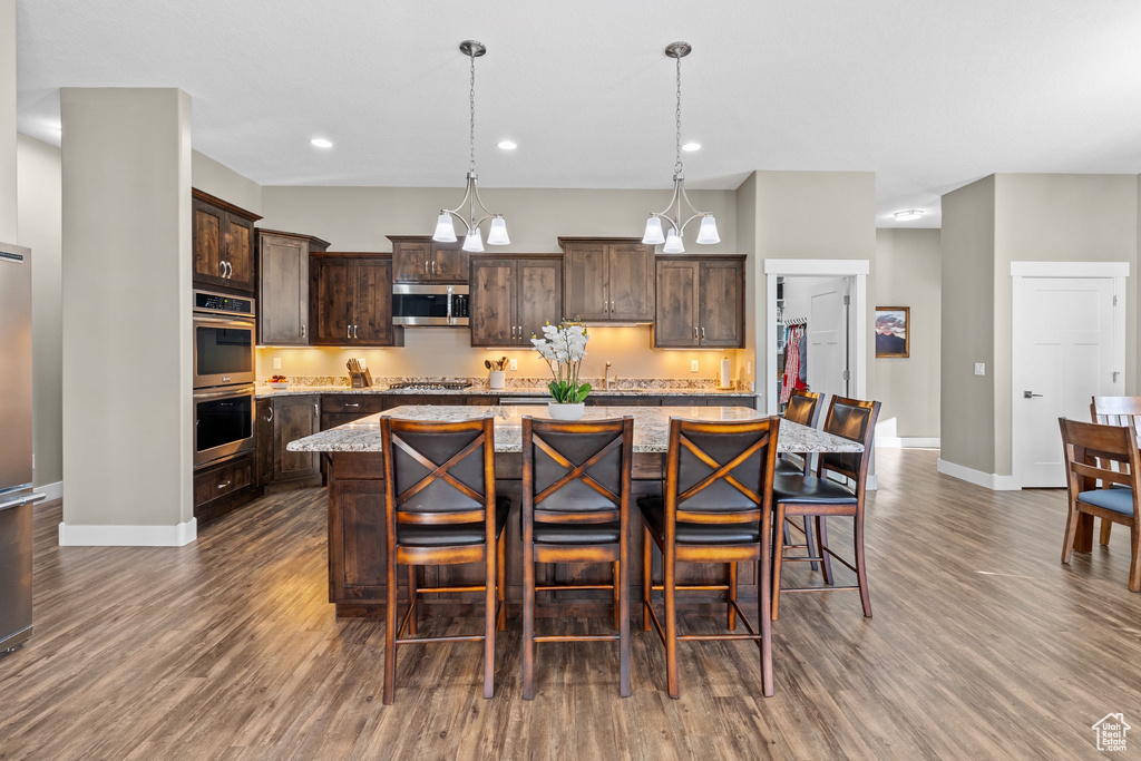 Kitchen with stainless steel appliances, dark wood-style floors, dark brown cabinetry, baseboards, and a center island