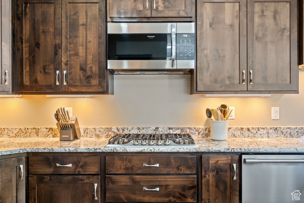 Kitchen featuring appliances with stainless steel finishes, dark brown cabinetry, and light stone counters