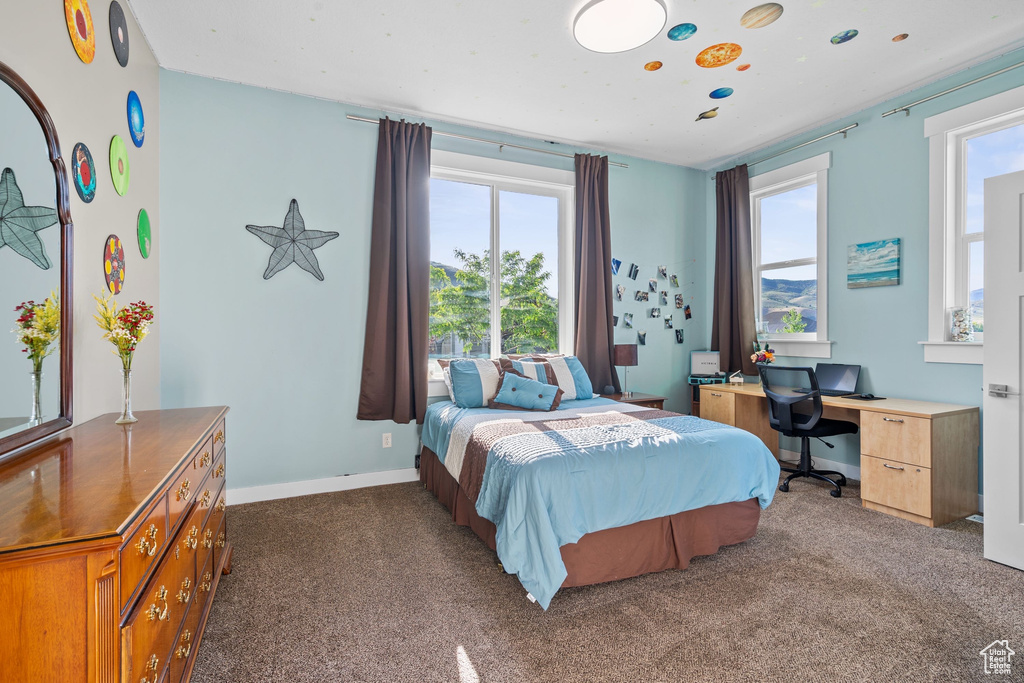 Bedroom with multiple windows, dark colored carpet, baseboards, and an office area