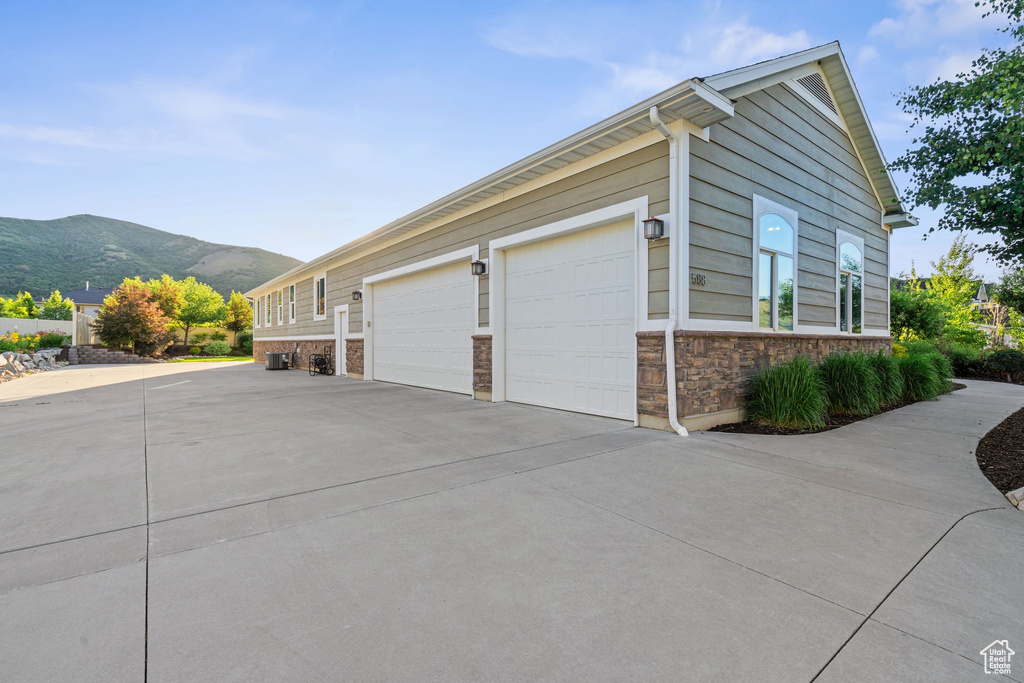 View of side of property with concrete driveway, a mountain view, and stone siding