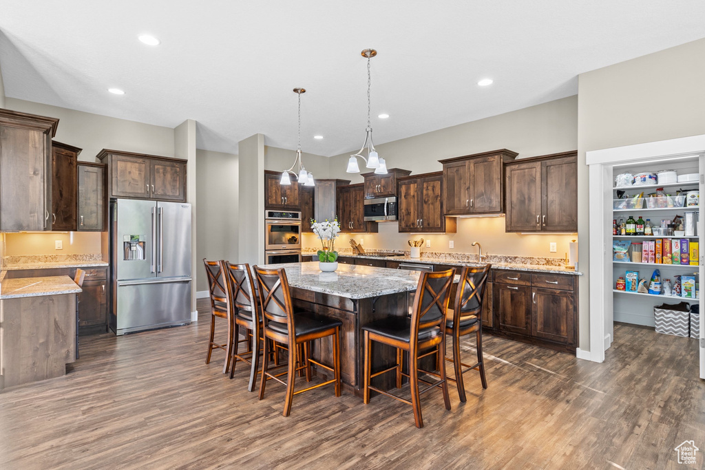 Kitchen featuring appliances with stainless steel finishes, dark brown cabinetry, a center island, dark wood-style floors, and recessed lighting