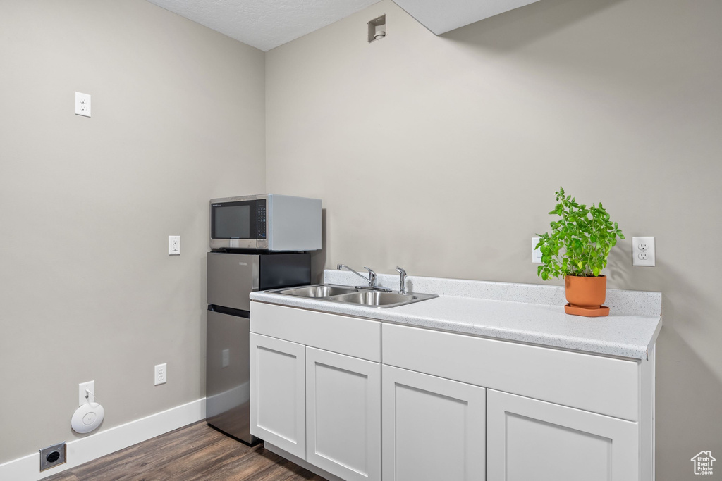 Kitchen with stainless steel microwave, a sink, white cabinets, dark wood-style flooring, and baseboards
