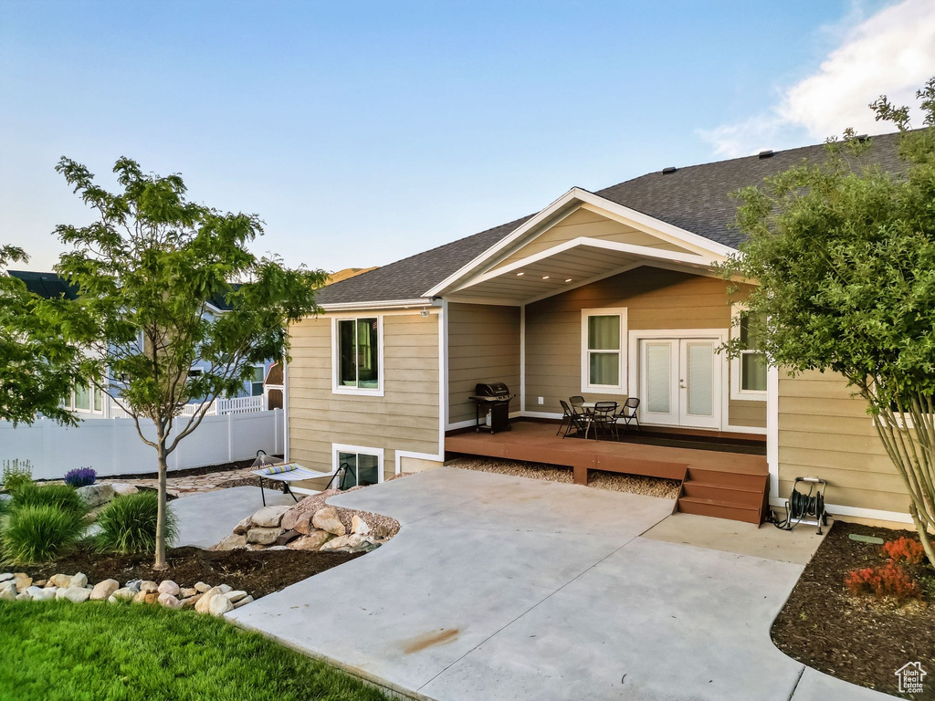 View of front of house featuring french doors, a wooden deck, a patio area, and roof with shingles