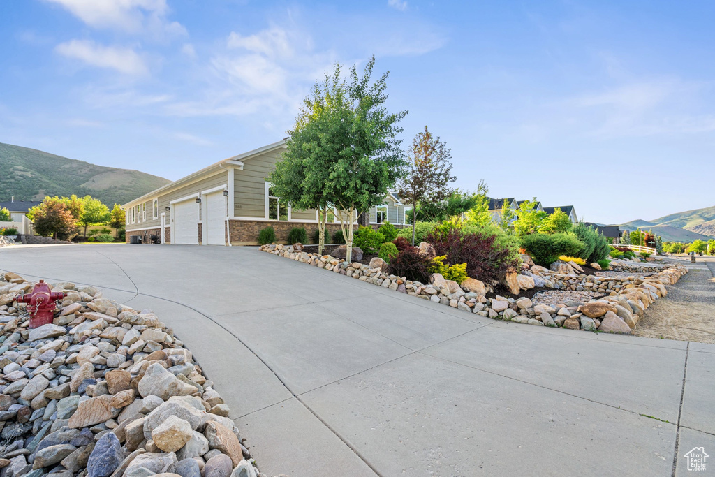 View of side of property featuring a mountain view, concrete driveway, an attached garage, and brick siding