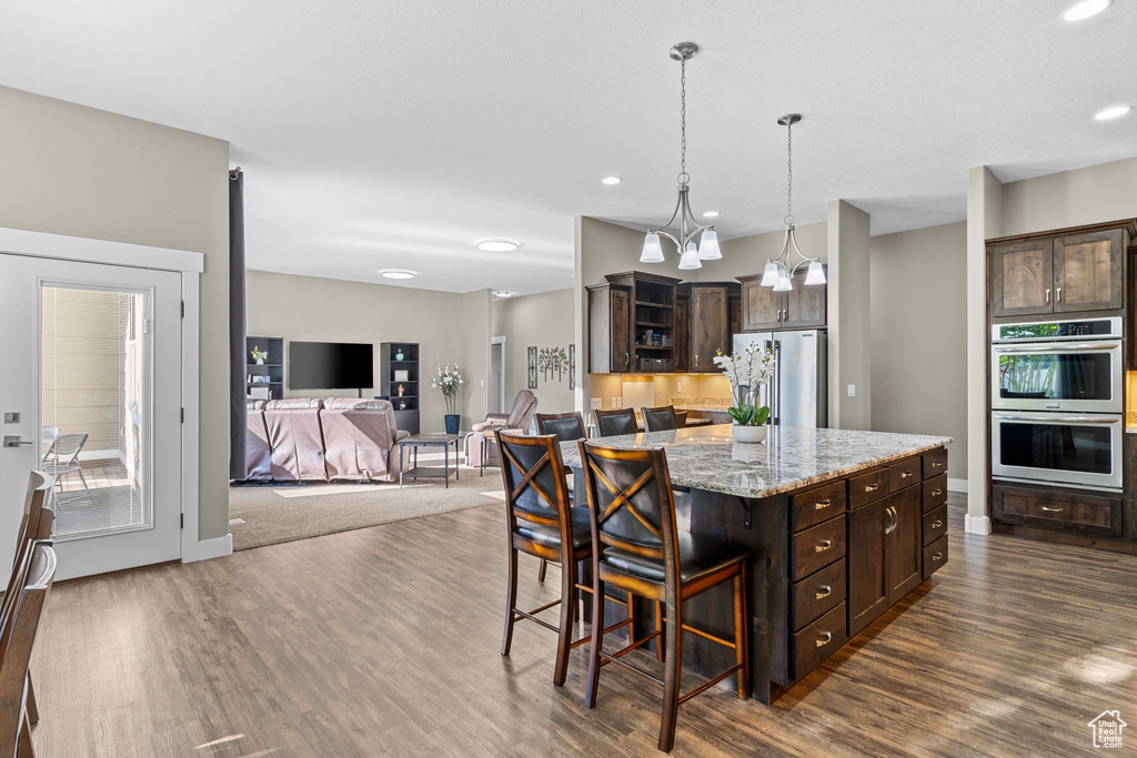 Kitchen featuring stainless steel appliances, dark brown cabinets, dark wood finished floors, a kitchen breakfast bar, and recessed lighting