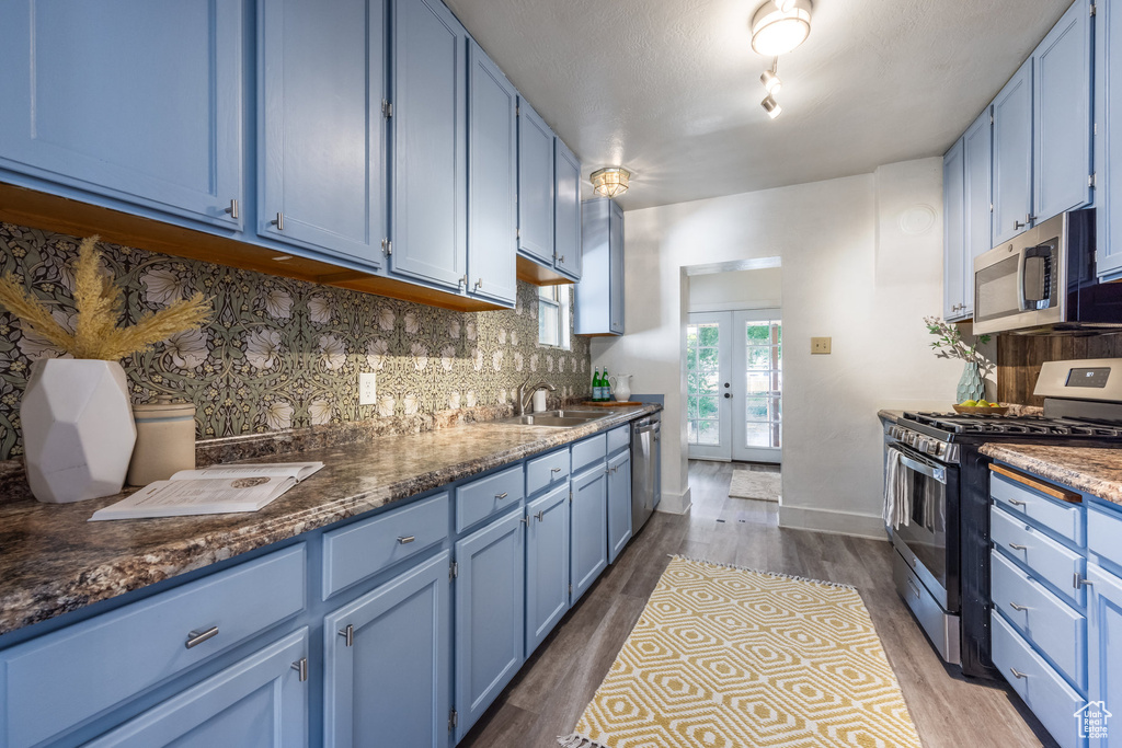 Kitchen with blue cabinetry, stainless steel appliances, a sink, decorative backsplash, and dark wood-type flooring