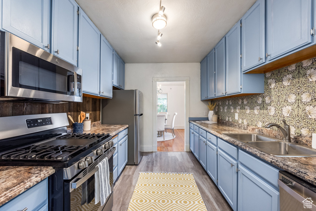 Kitchen with appliances with stainless steel finishes, blue cabinets, a sink, light wood-style flooring, and tasteful backsplash