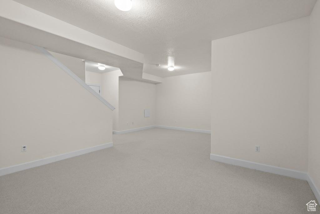 Finished basement featuring light carpet, baseboards, and a textured ceiling