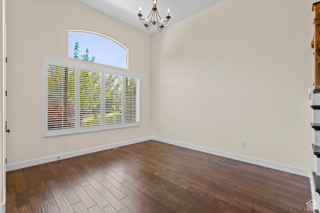 Spare room featuring a chandelier, dark wood-type flooring, high vaulted ceiling, and baseboards
