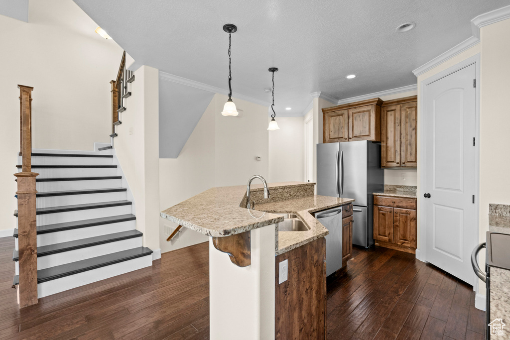 Kitchen with a sink, appliances with stainless steel finishes, brown cabinetry, dark wood-style flooring, and crown molding