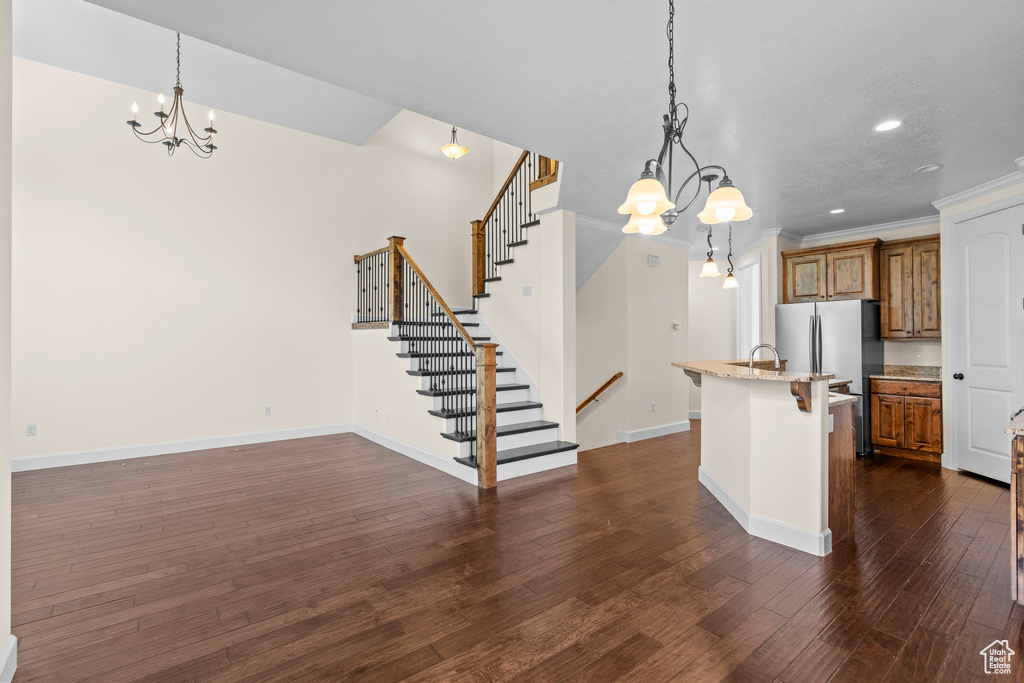 Kitchen featuring a chandelier, brown cabinetry, freestanding refrigerator, dark wood-type flooring, and light stone counters