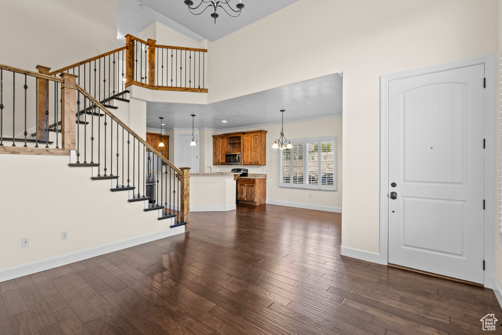 Foyer entrance featuring a chandelier, a towering ceiling, dark wood finished floors, stairs, and baseboards