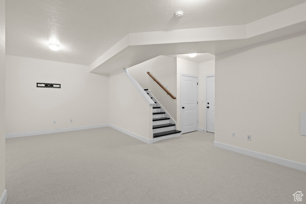 Below grade area featuring light carpet, baseboards, a textured ceiling, and stairs
