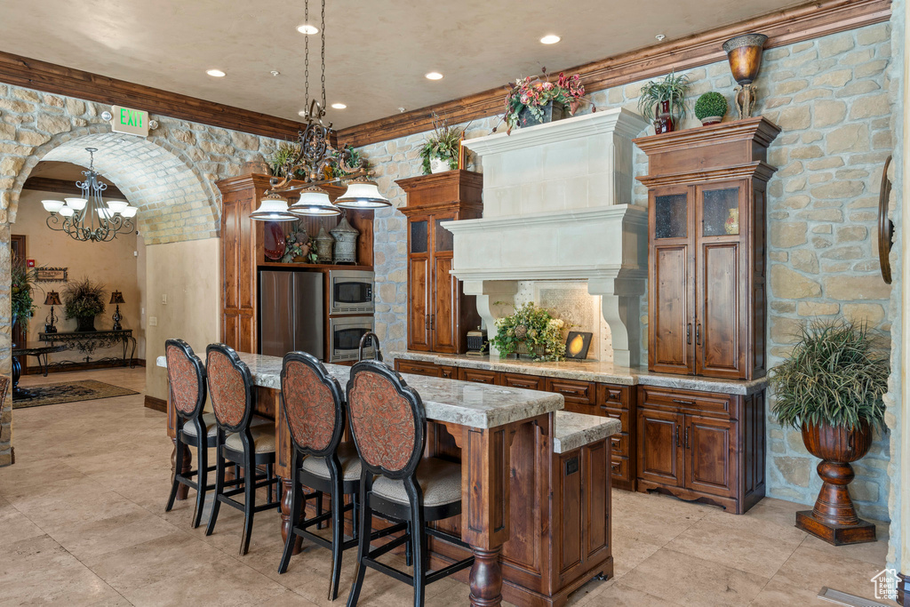 Kitchen with appliances with stainless steel finishes, a chandelier, a kitchen bar, a center island with sink, and brown cabinets