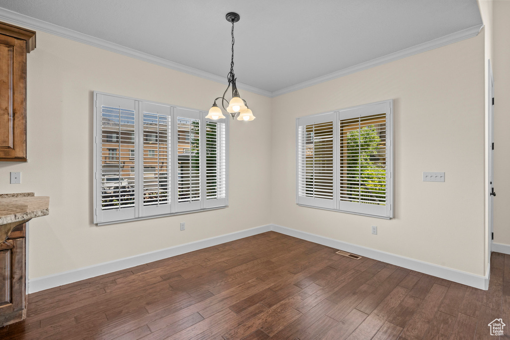 Unfurnished dining area featuring ornamental molding, a chandelier, healthy amount of natural light, baseboards, and dark wood-style flooring