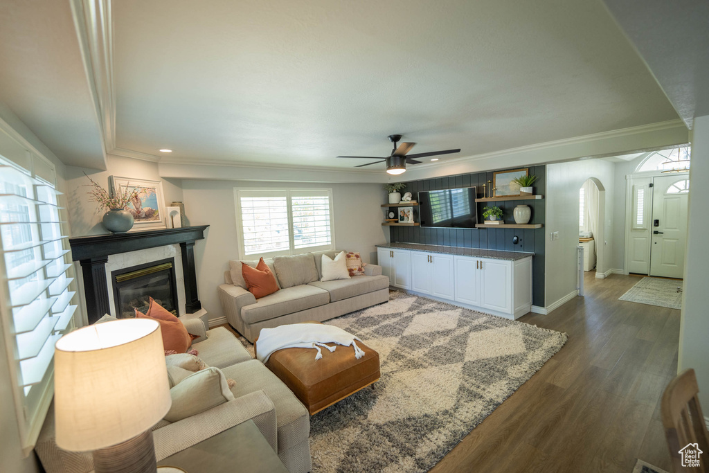 Living area featuring arched walkways, a ceiling fan, dark wood finished floors, crown molding, and baseboards