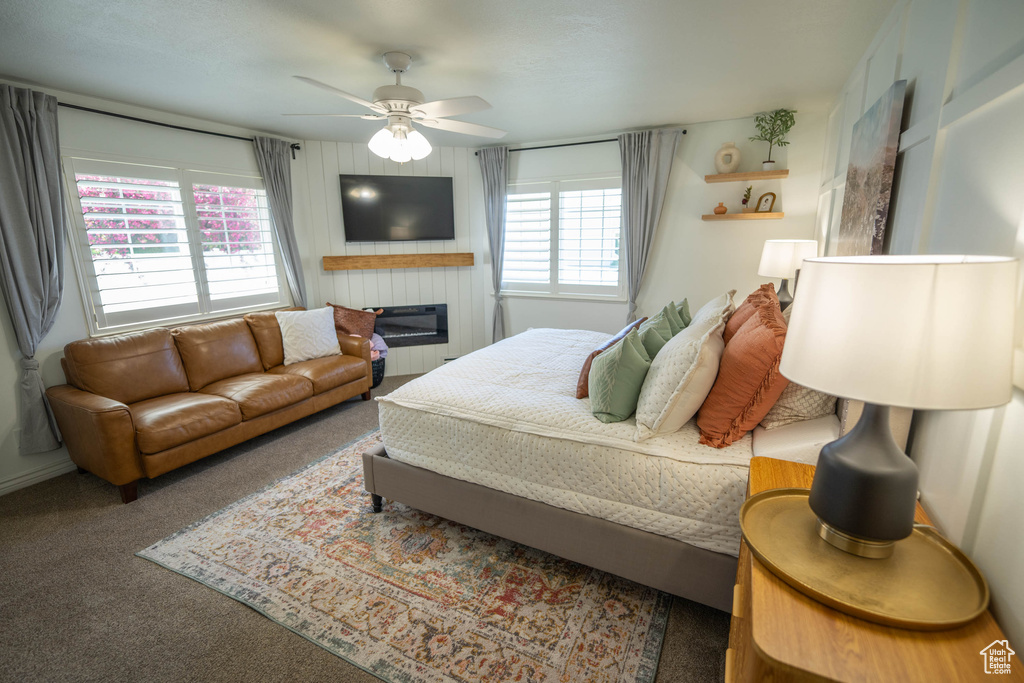Carpeted bedroom with ceiling fan and a glass covered fireplace