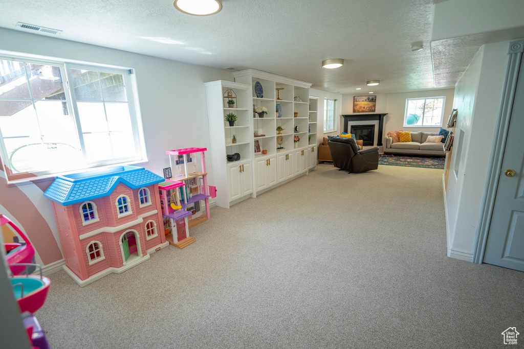 Playroom with carpet floors, a textured ceiling, and a glass covered fireplace