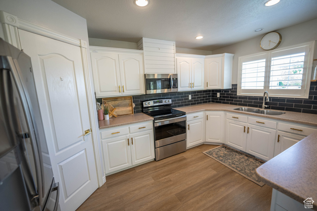 Kitchen featuring stainless steel appliances, a sink, tasteful backsplash, light wood finished floors, and recessed lighting
