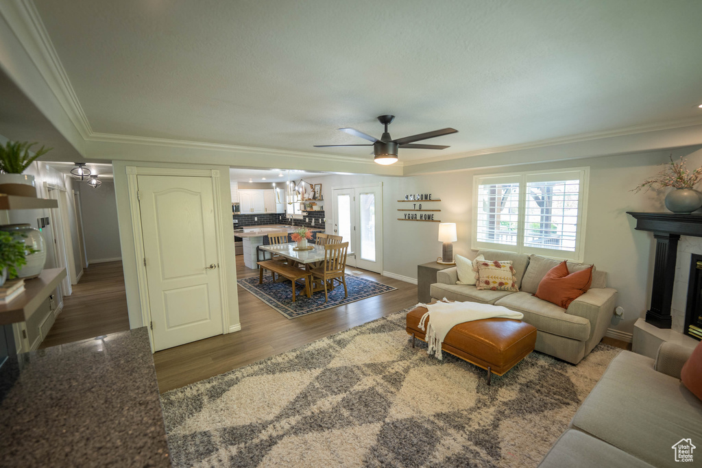 Living room featuring ceiling fan, crown molding, wood finished floors, a tiled fireplace, and baseboards