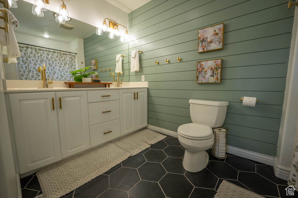 Full bath with double vanity, toilet, baseboards, wooden walls, and tile patterned flooring