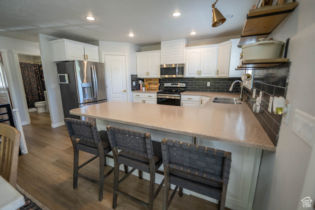 Kitchen with appliances with stainless steel finishes, a sink, a peninsula, decorative backsplash, and a breakfast bar