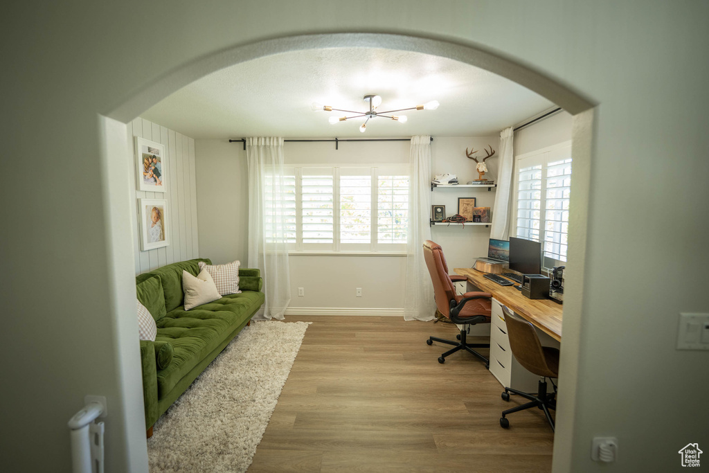 Office space featuring arched walkways, light wood-style floors, a chandelier, and baseboards