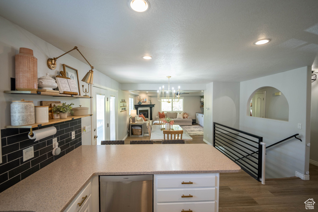 Kitchen featuring dishwasher, white cabinetry, wood finished floors, a chandelier, and tasteful backsplash