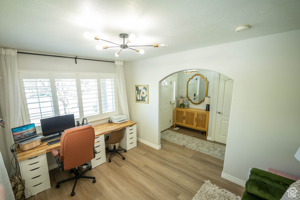 Office space with a chandelier, light wood-style floors, baseboards, and arched walkways