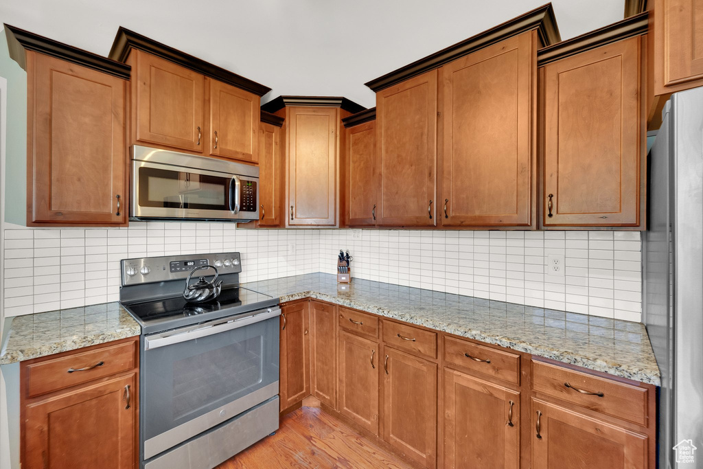 Kitchen with stainless steel appliances, light wood finished floors, light stone counters, and backsplash