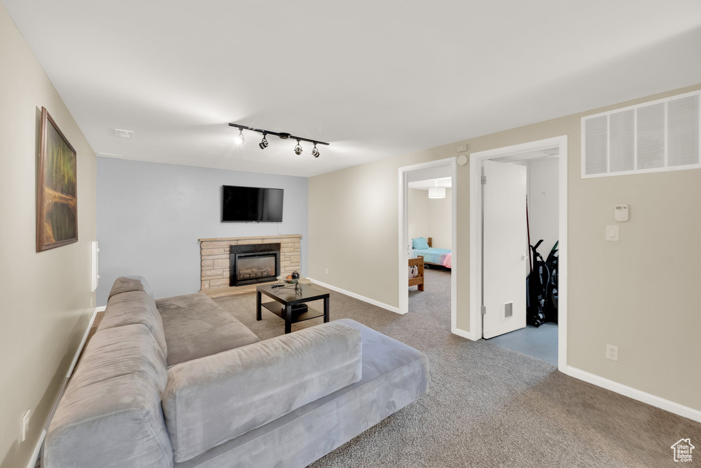 Carpeted living area featuring rail lighting, a stone fireplace, and baseboards