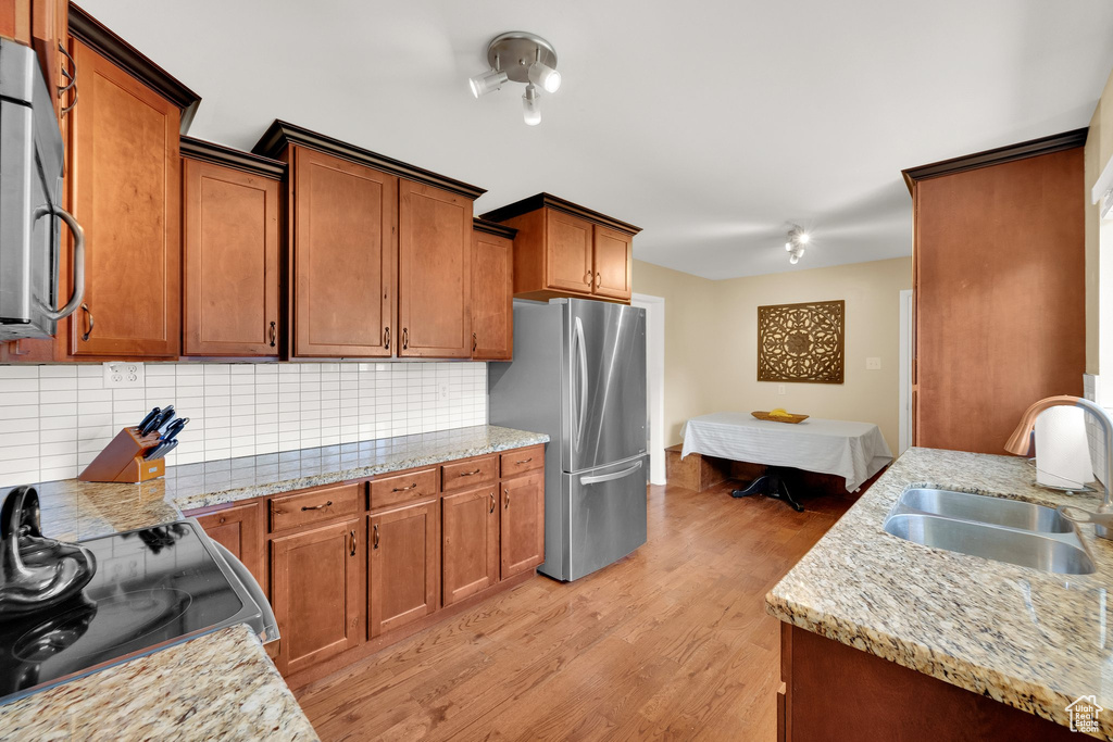 Kitchen with appliances with stainless steel finishes, a sink, backsplash, light wood finished floors, and brown cabinets