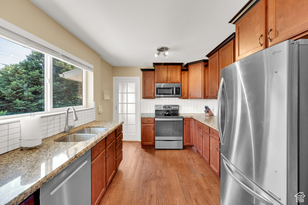 Kitchen with appliances with stainless steel finishes, a sink, light wood-type flooring, and backsplash