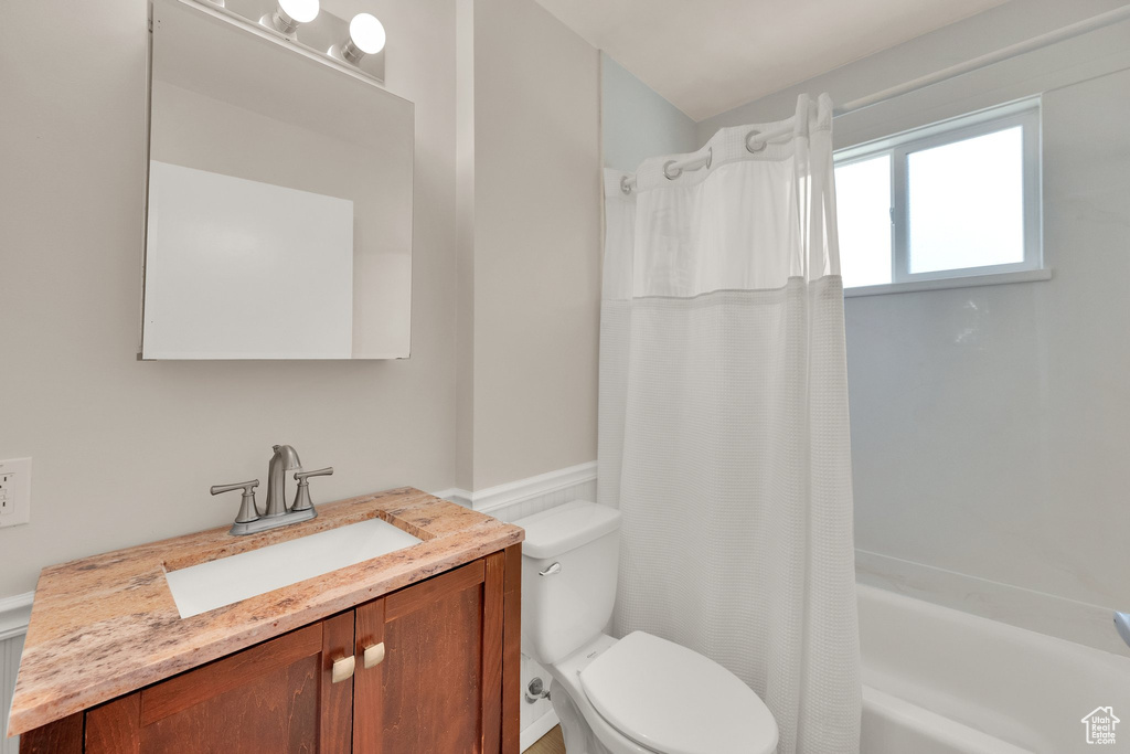 Bathroom with toilet, shower / bath combo, vanity, and wainscoting