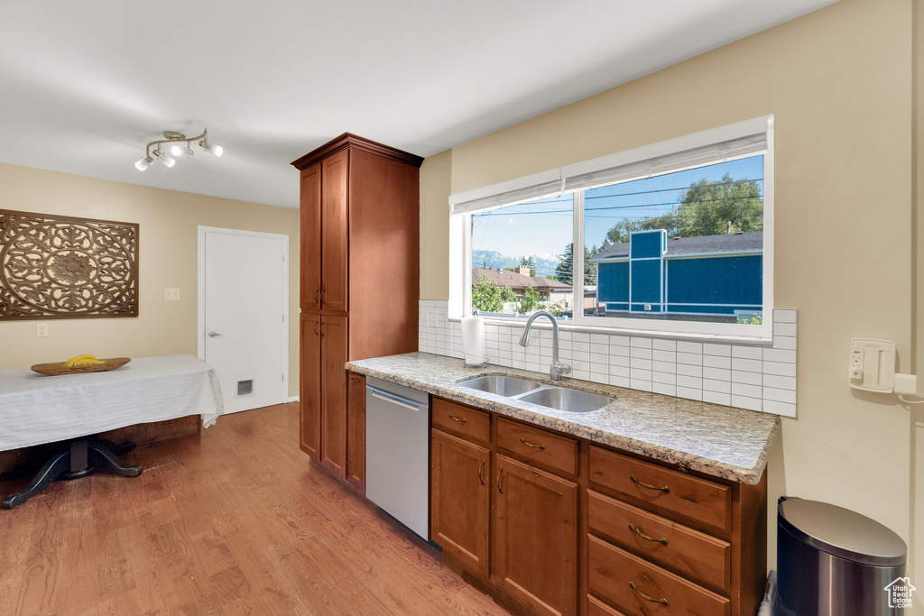 Kitchen featuring dishwasher, a sink, tasteful backsplash, light wood finished floors, and brown cabinetry