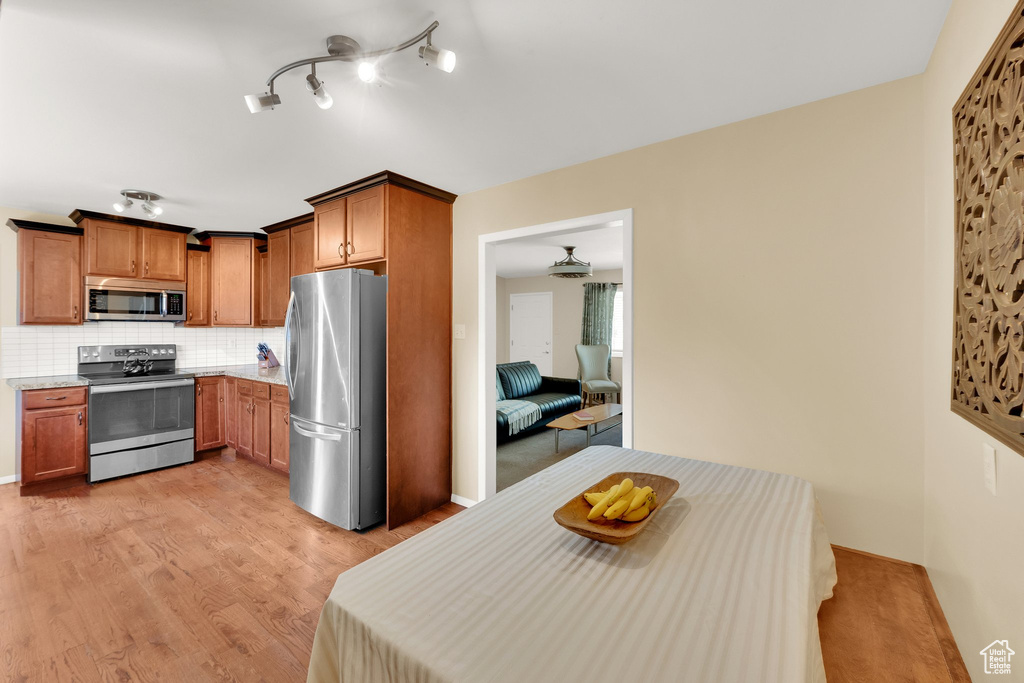 Kitchen featuring appliances with stainless steel finishes, light wood-type flooring, decorative backsplash, and brown cabinets